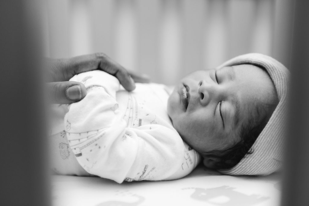 A black and white portrait of a newborn baby sleeping in a crib.