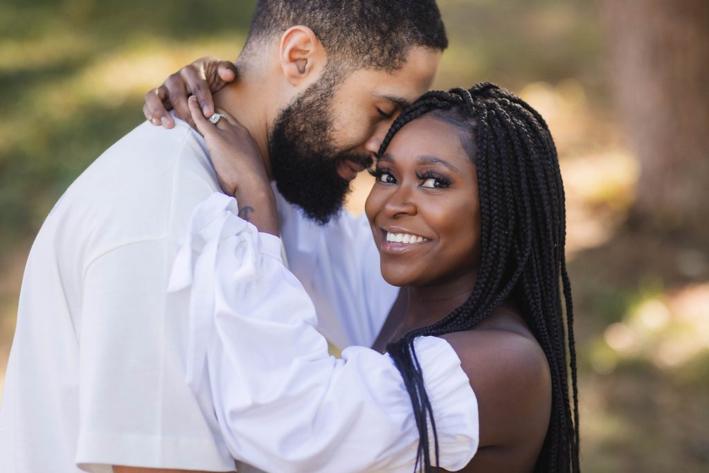 A black couple embracing in the woods during their engagement session.