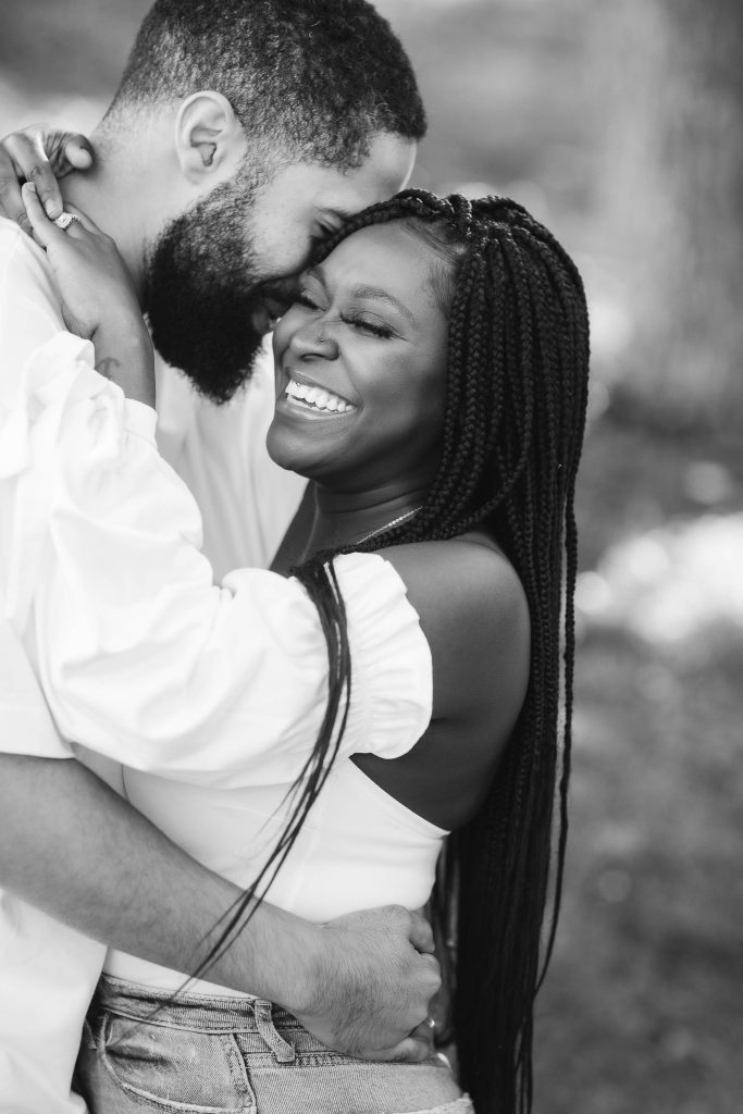 A black and white photo of an engaged couple hugging in their family home.