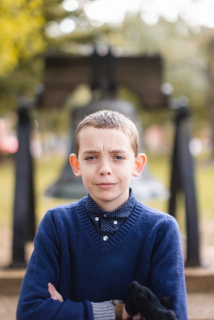 A boy with his arms crossed in front of a downtown Annapolis bell.