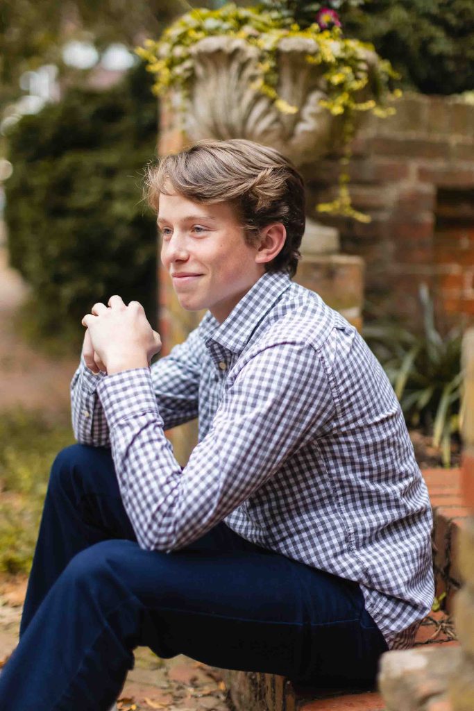 A young man in a plaid shirt posing for a portrait on a brick wall in downtown Annapolis.