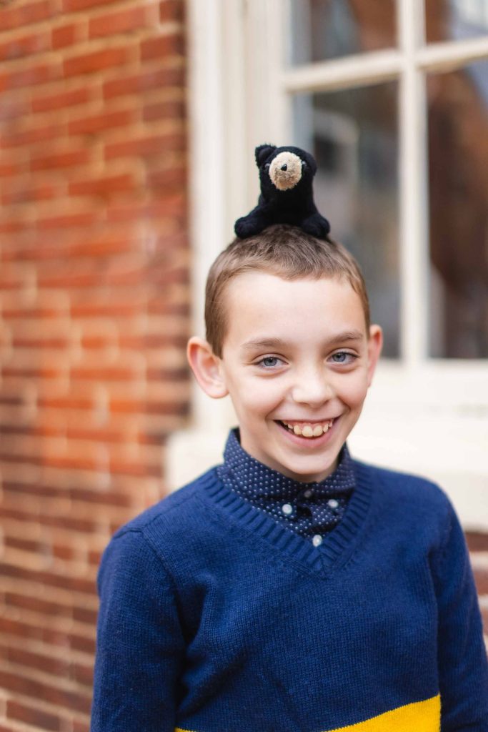 A boy, wearing a hat adorned with a bear, captured in a portrait amidst the scenic backdrop of Downtown Annapolis.