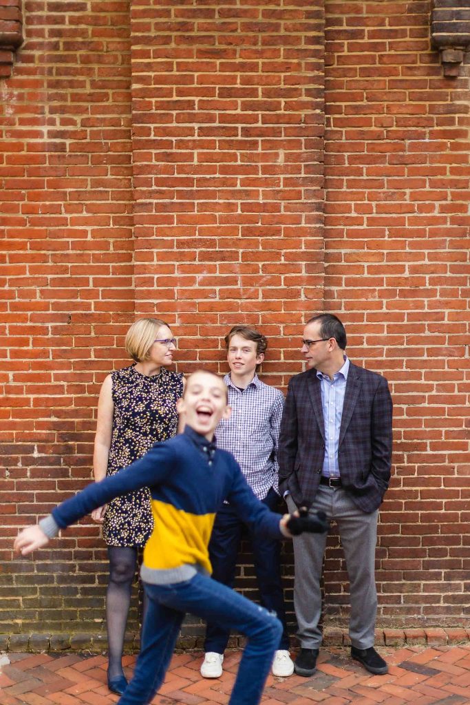 A family is standing in front of a downtown Annapolis brick wall, capturing timeless portraits.