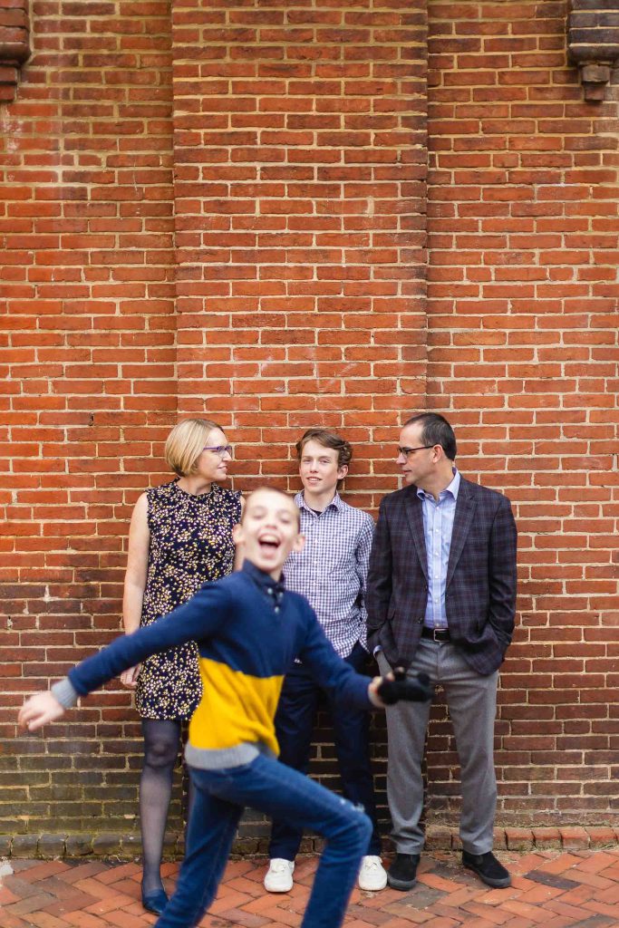 A family is standing in front of a downtown Annapolis brick wall, capturing timeless portraits.