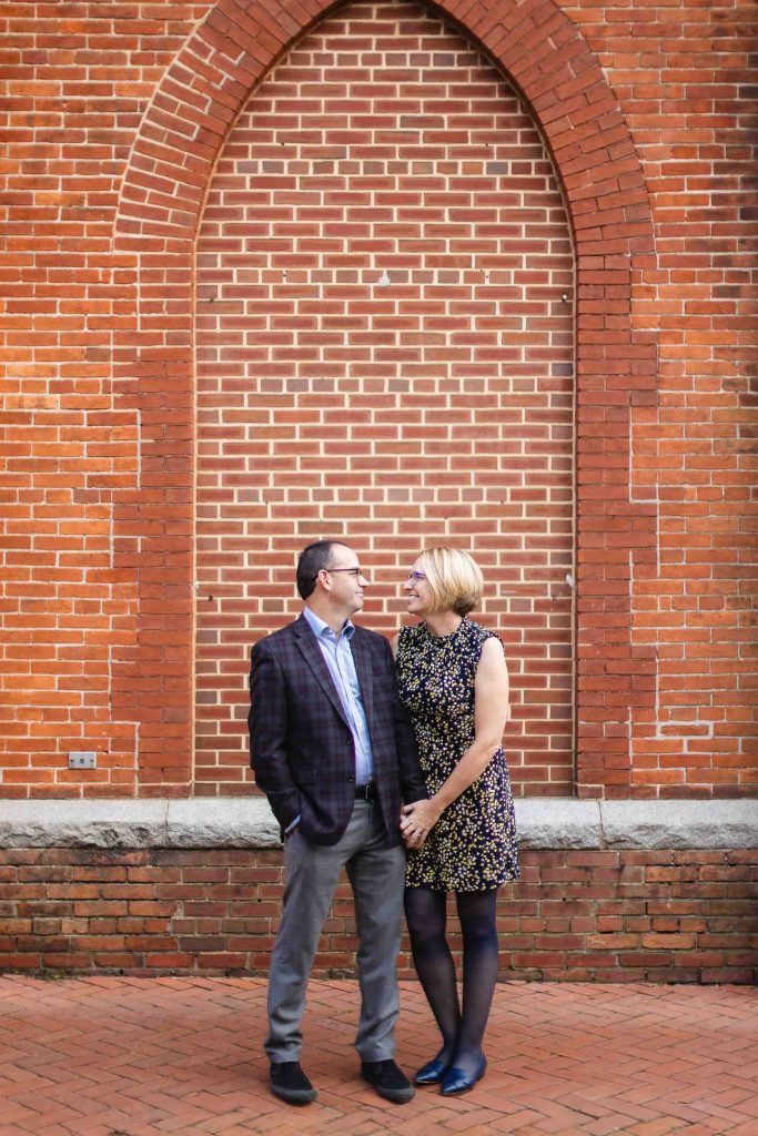 A portrait of an engaged couple standing in front of a brick wall in downtown Annapolis.