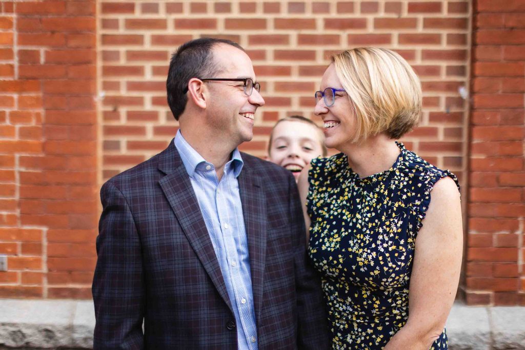 A smiling man and woman are posing for portraits in front of a brick building in downtown Annapolis.