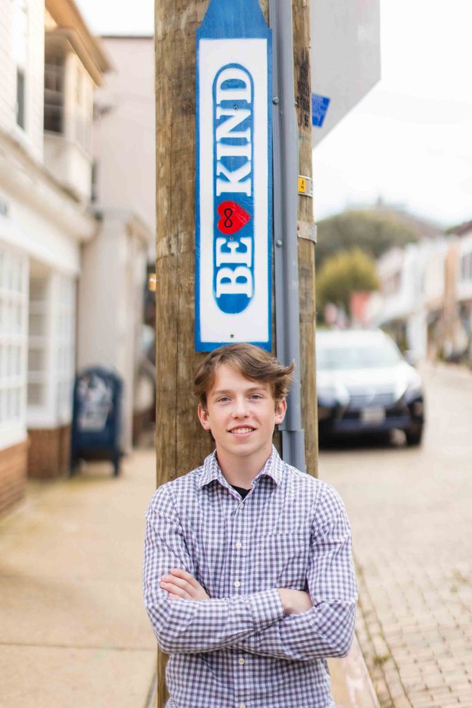 A young man standing next to a sign that says be kind in downtown Annapolis.