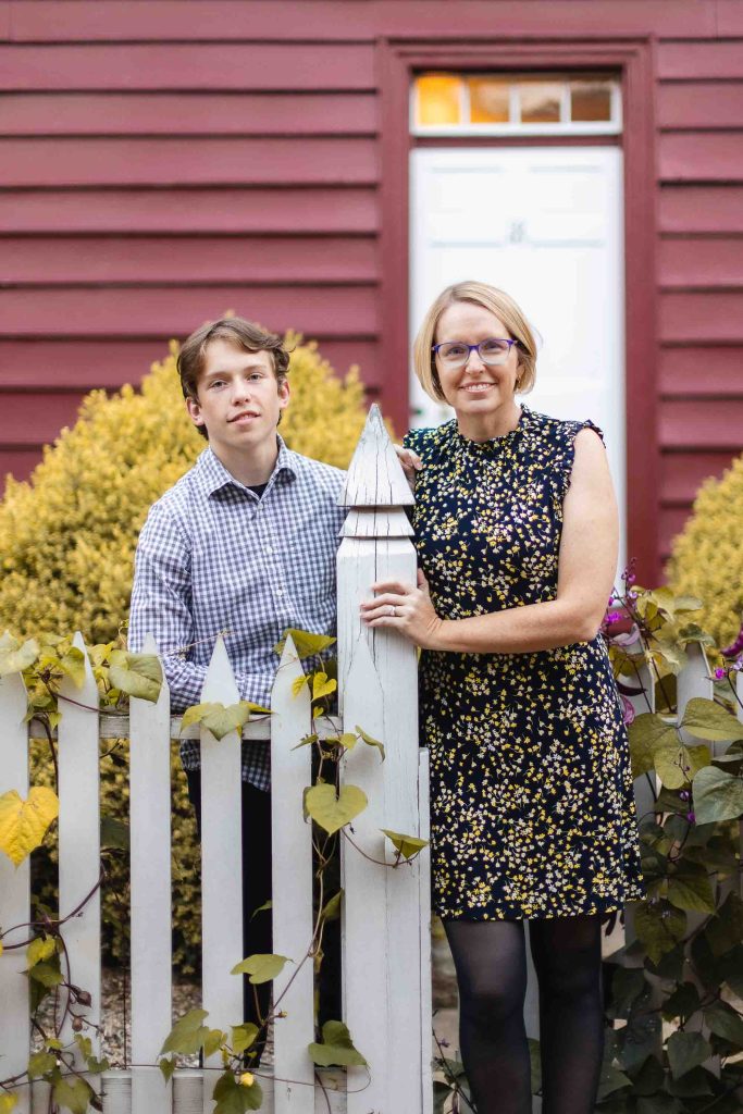 A man and woman standing next to a white picket fence in front of a red house, capturing the essence of family.