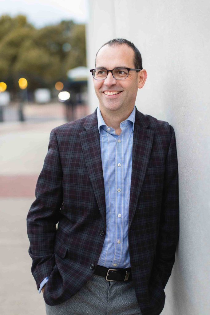A man in glasses is leaning against a wall in Downtown Annapolis.