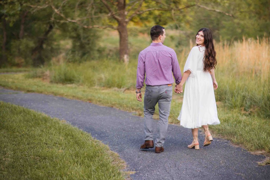 An engaged couple walking down a path in the beautiful Patuxent Research Refuge in Maryland, surrounded by the stunning sunset.