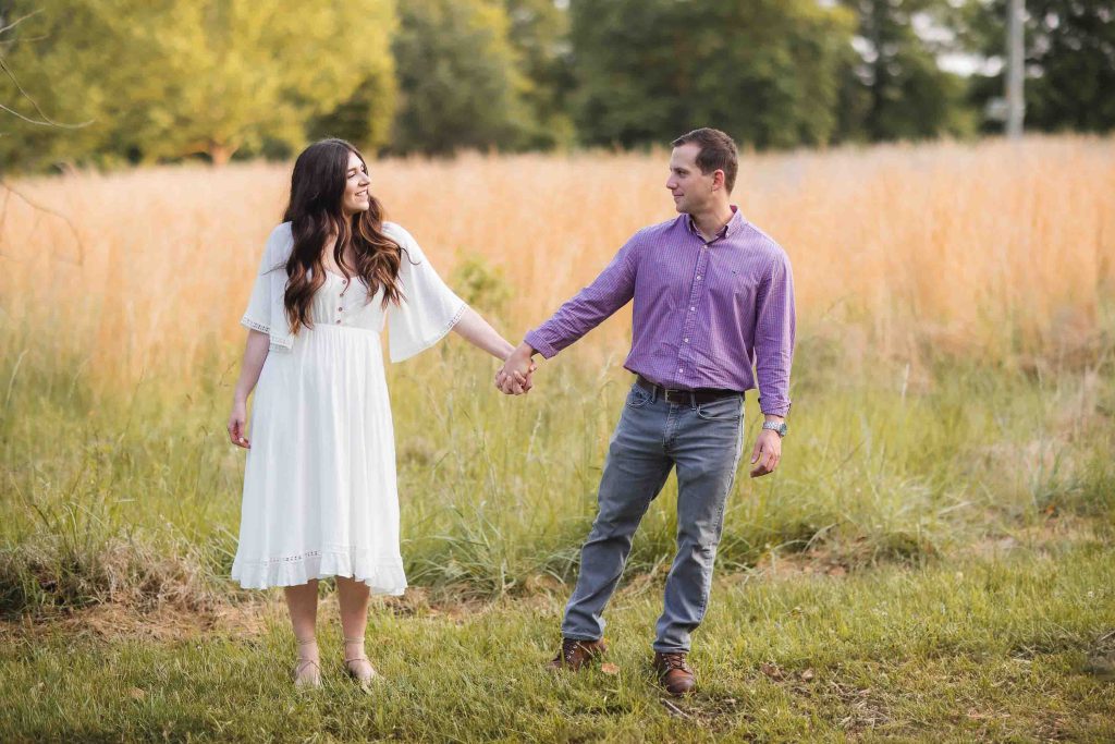 An engaged couple holding hands in a field at Patuxent Research Refuge, capturing their beautiful connection as the sun sets for their engagement photos.