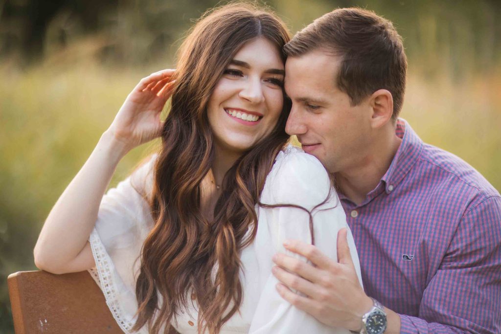 A couple is embracing on a bench in Maryland's Patuxent Research Refuge, capturing beautiful engagement photos amidst the scenic field.