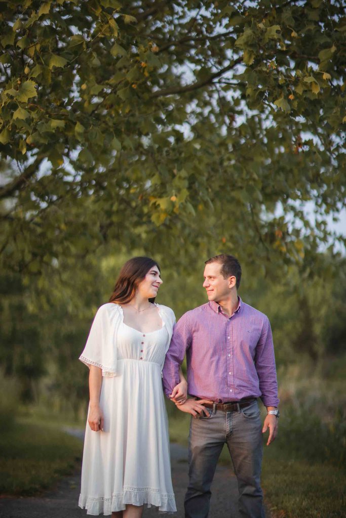 An engaged couple standing next to each other in a park at sunset, capturing beautiful engagement photos in Maryland.