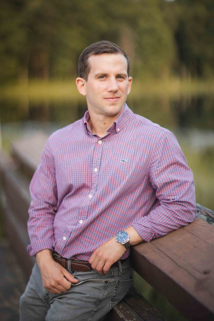 A man in a striped shirt leaning on a railing near Patuxent Research Refuge at sunset.