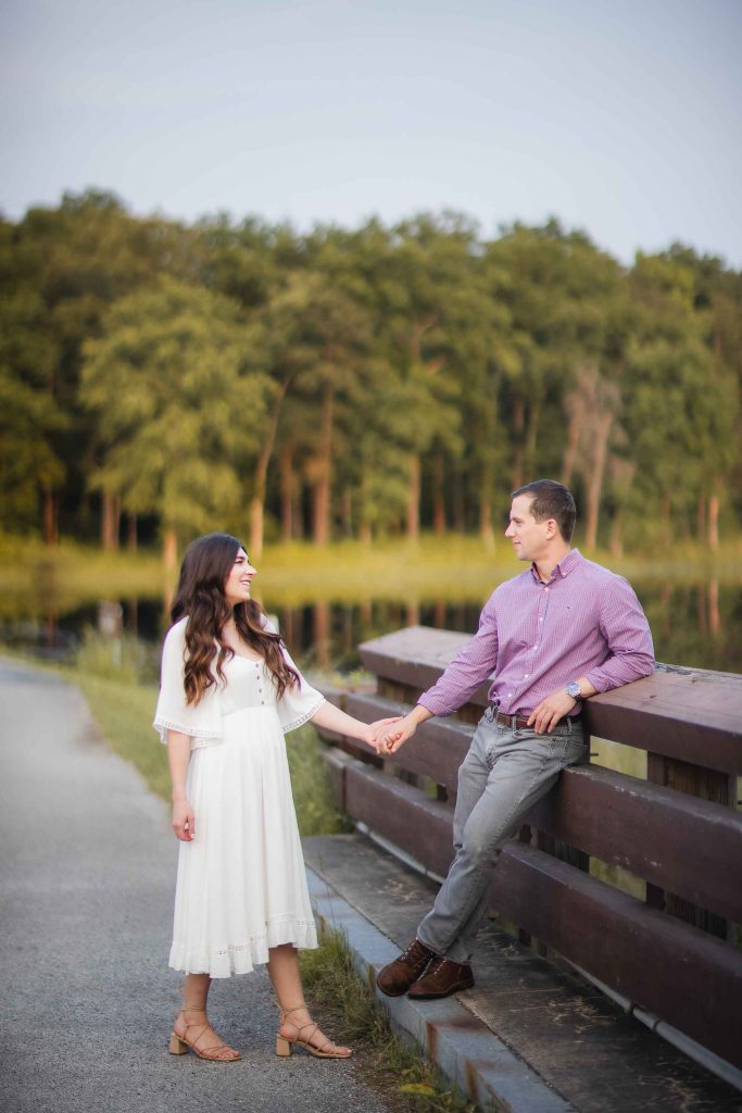 An engaged couple holding hands on a wooden bench near Patuxent Research Refuge in Maryland.