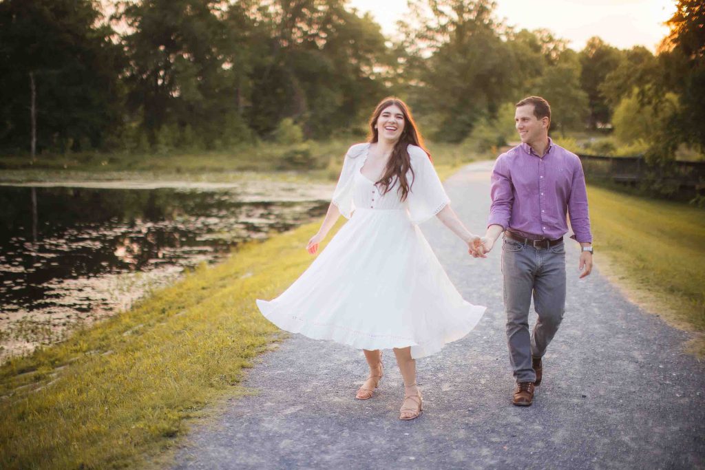 An engaged couple taking romantic engagement photos near a scenic pond in Maryland during a breathtaking sunset.