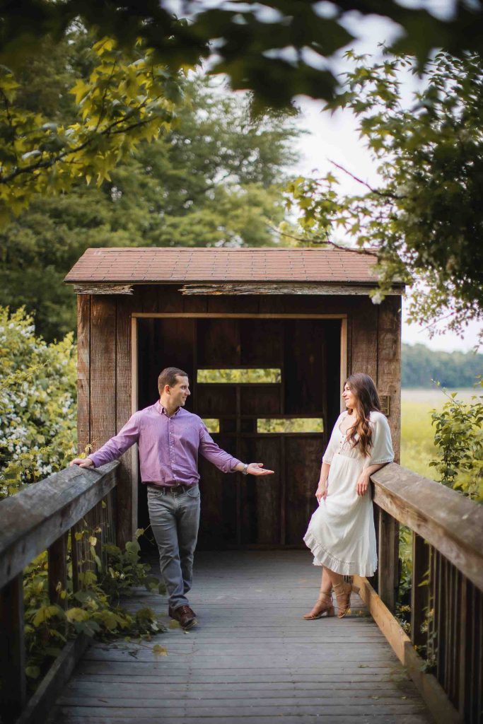 An engaged couple standing on a wooden bridge, capturing their romantic Maryland engagement photos as the mesmerizing sunset adds a touch of magic to the scene.