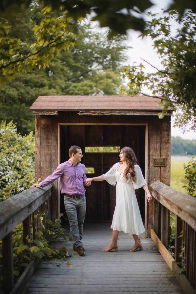 An engaged couple standing on a wooden bridge in the woods during a sunset in Maryland.