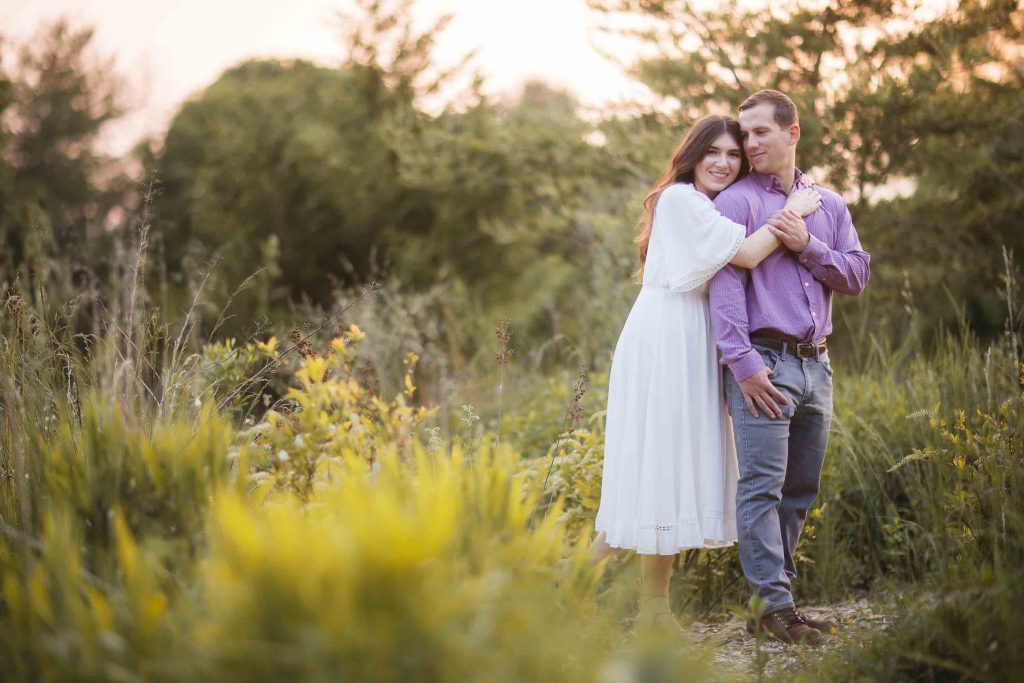 A couple embraces in the tall grass at Patuxent Research Refuge during their engagement session at sunset.