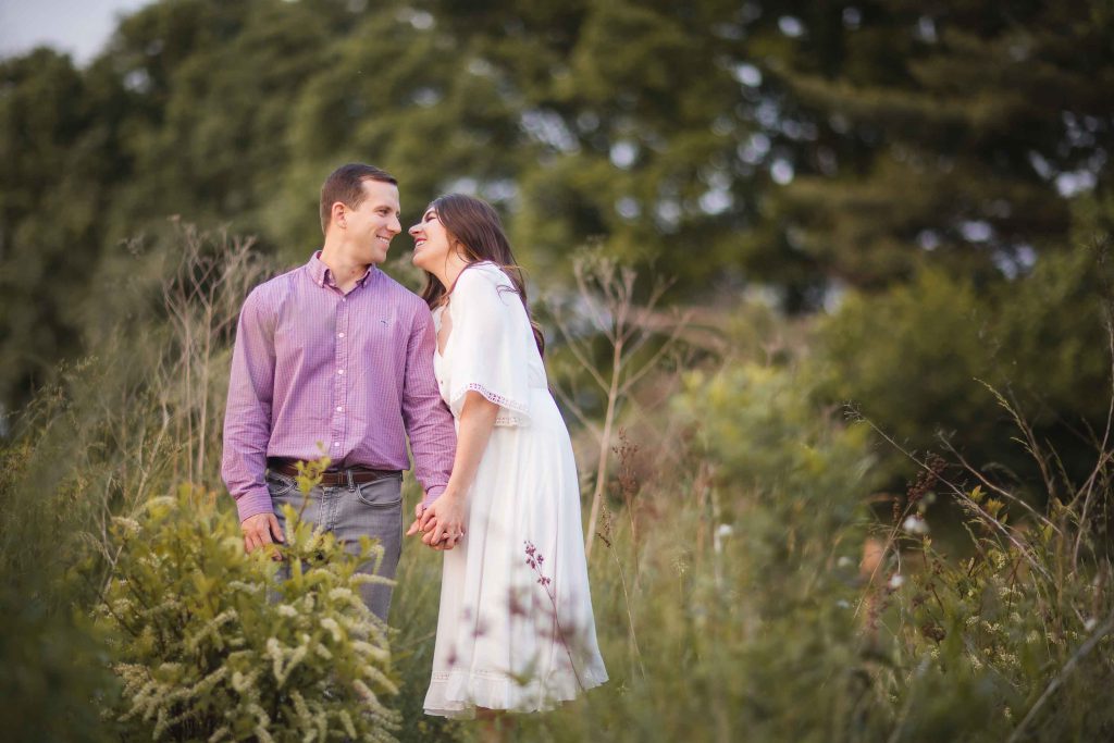 An engaged couple standing in tall grass during sunset in Maryland, capturing beautiful engagement photos.