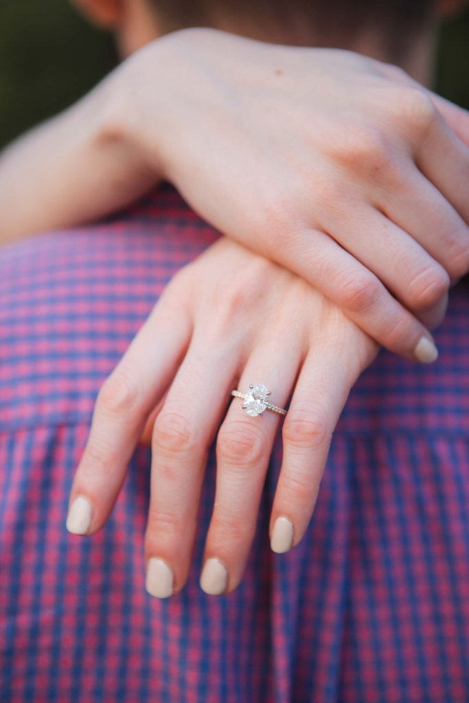 A breathtaking engagement ring glimmers on a woman's hand as the mesmerizing Maryland sunset bathes their love in warm hues.