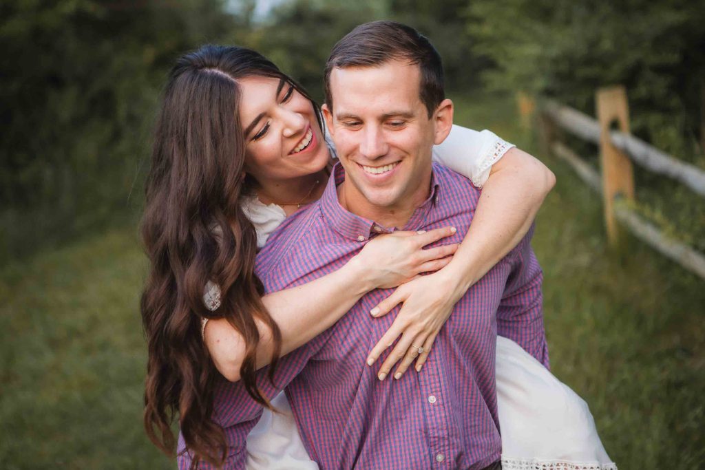 A man and woman embracing in the Patuxent Research Refuge field, capturing their love during a breathtaking sunset for their engagement photos.