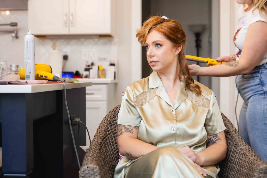 A bride-to-be is getting her hair done in a kitchen as part of her wedding preparation.
