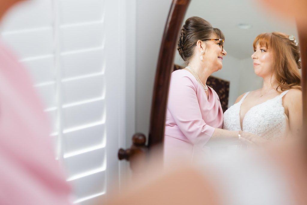 A bride and her mother sharing a heartfelt moment during their wedding preparation, gazing at each other in the mirror.