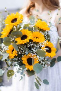 Wedding details: A bride holding a bouquet of sunflowers and eucalyptus.