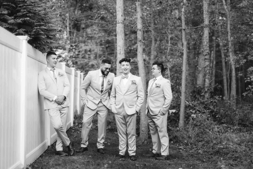 Keywords: Wedding, Groomsmen. 

Description: Groomsmen standing next to a fence in the woods at a wedding.
