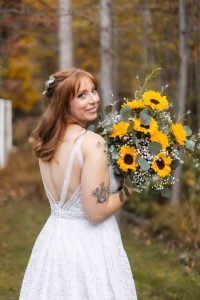 A bride holding sunflowers in a wooded area at her wedding.