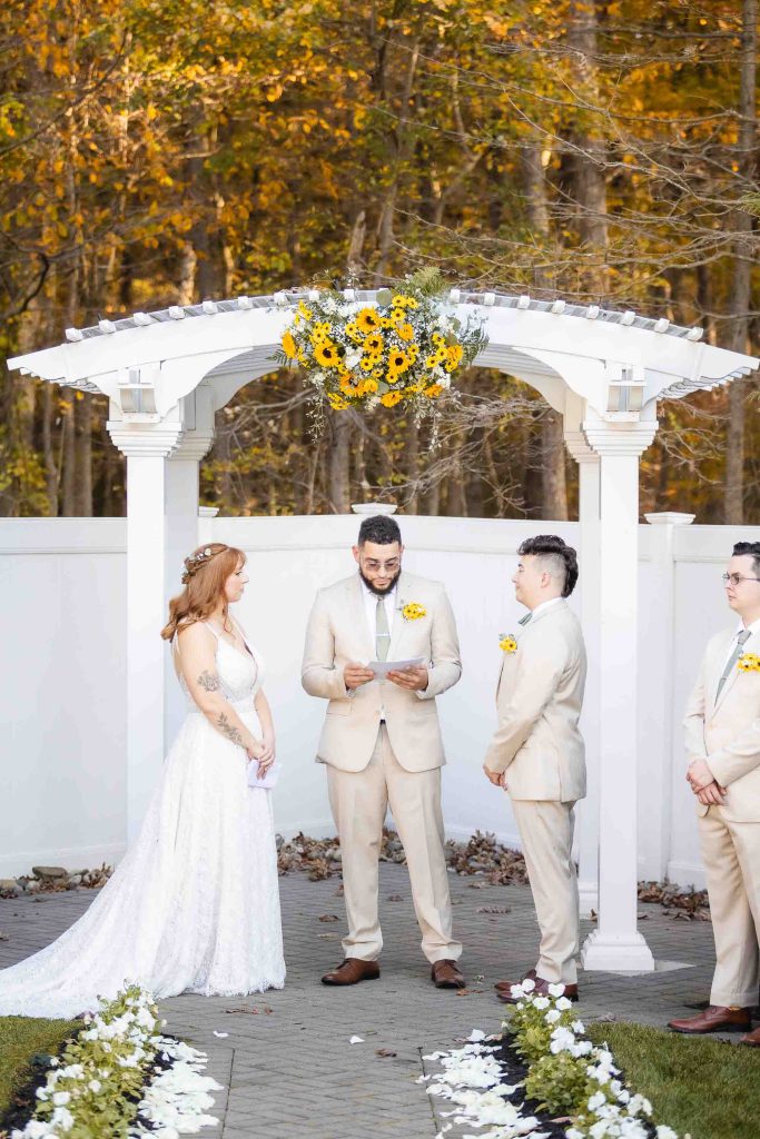 A Blackwall Barn & Lodge wedding ceremony with the bride and groom in front of a gazebo adorned with sunflowers.