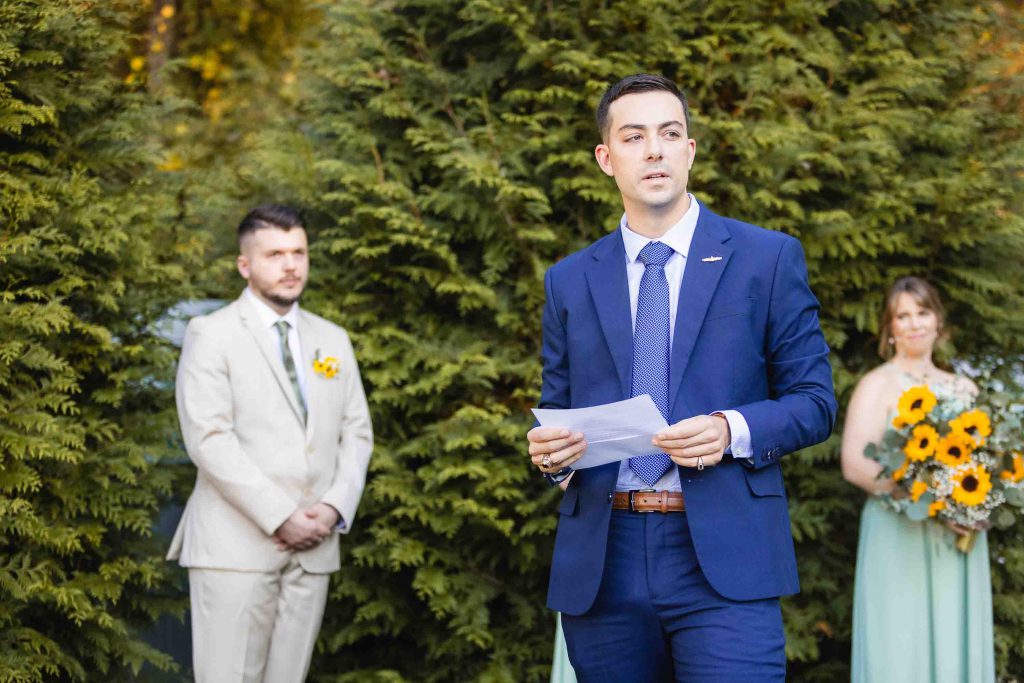 At the Blackwall Barn & Lodge wedding ceremony, a man in a suit is reading a letter to the bride and groom.