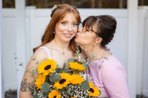 A Wedding Portrait captures a bride and her mother sharing an intimate kiss amidst a picturesque backdrop of sunflowers at the serene Blackwall Barn & Lodge.
