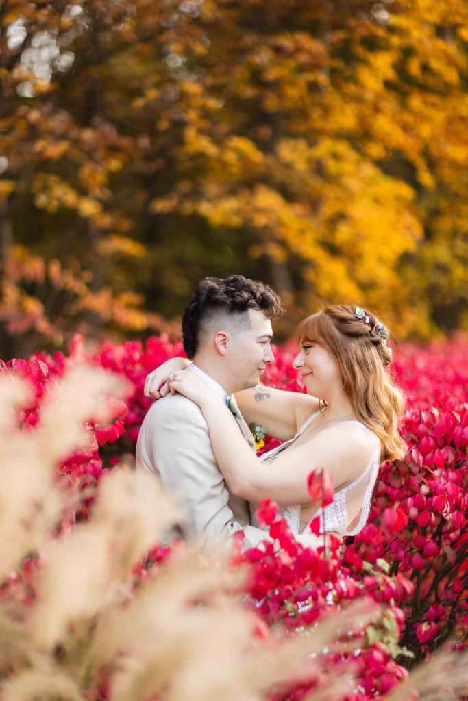A wedding portrait of a bride and groom embracing in a field of red flowers at Blackwall Barn & Lodge.