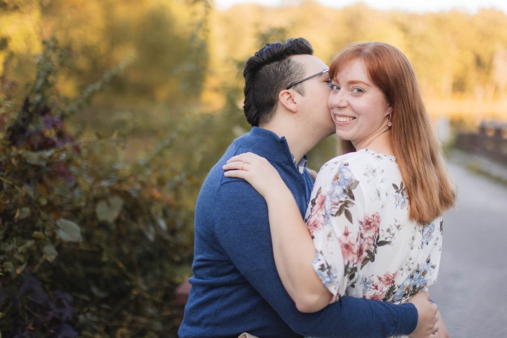 An engaged couple embraces in front of a tree at Patuxent Research Refuge, capturing beautiful portraits.
