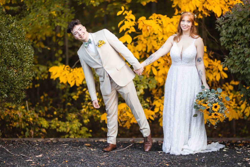 A bride and groom holding hands in front of a yellow tree at their wedding ceremony.