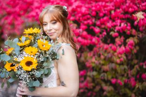 A bride holding a bouquet of sunflowers in front of a red bush at her wedding at Blackwall Barn & Lodge.