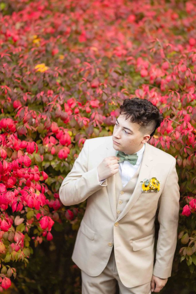 A man in a tuxedo standing in a field of red flowers, capturing an elegant portrait.