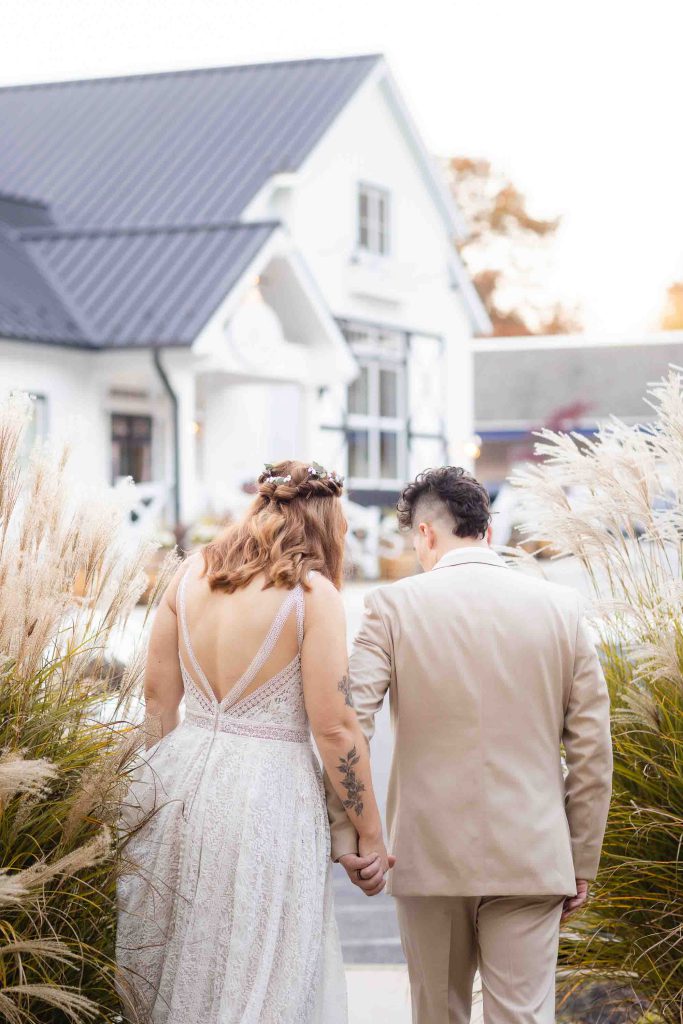 A Blackwall Barn & Lodge wedding portrait of a bride and groom holding hands in front of a white house.
