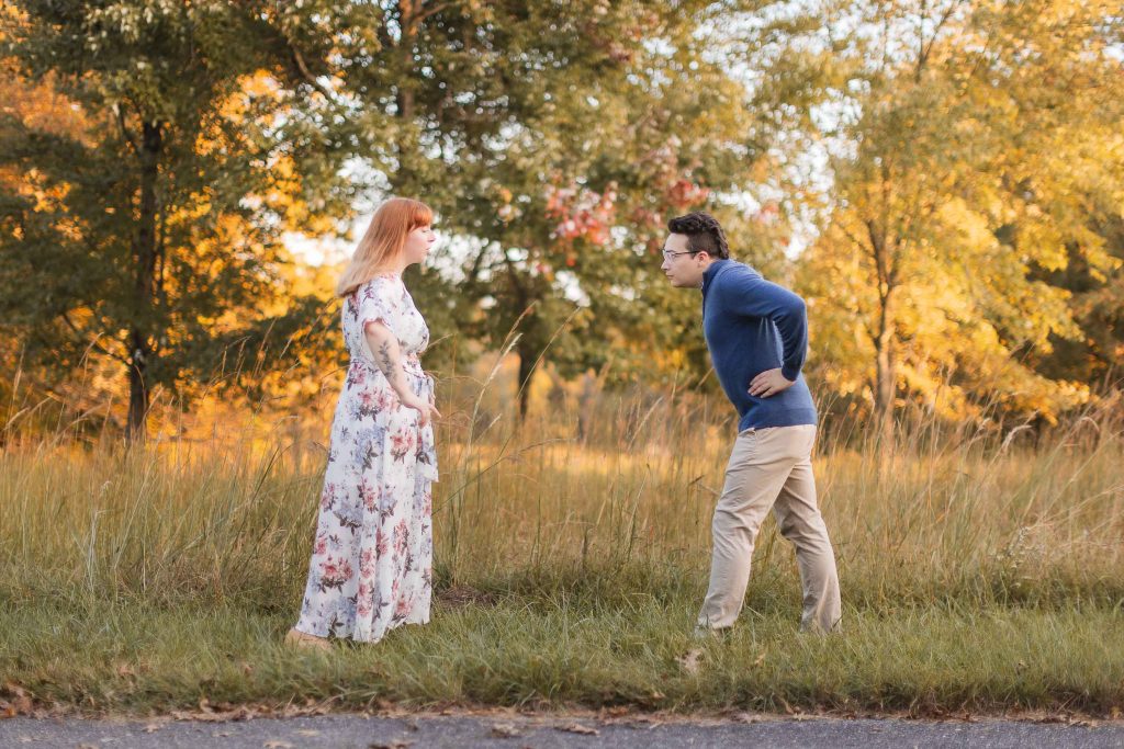 A man and woman are standing in the middle of a field in the fall, capturing engagement portraits at Patuxent Research Refuge.
