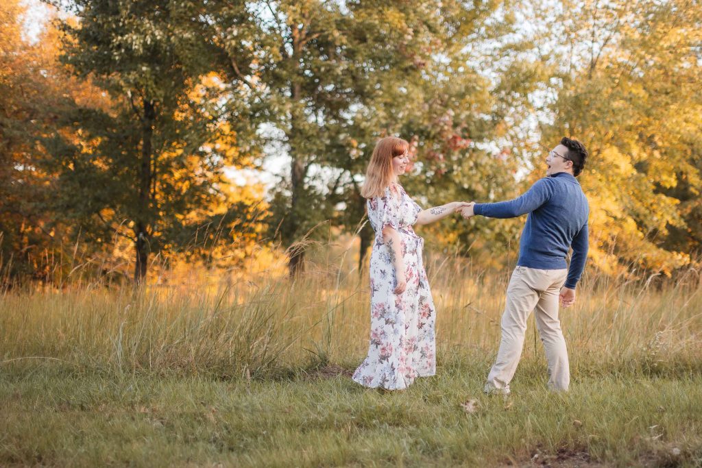 A man and woman standing in a field at Patuxent Research Refuge, holding hands in an engagement portrait.