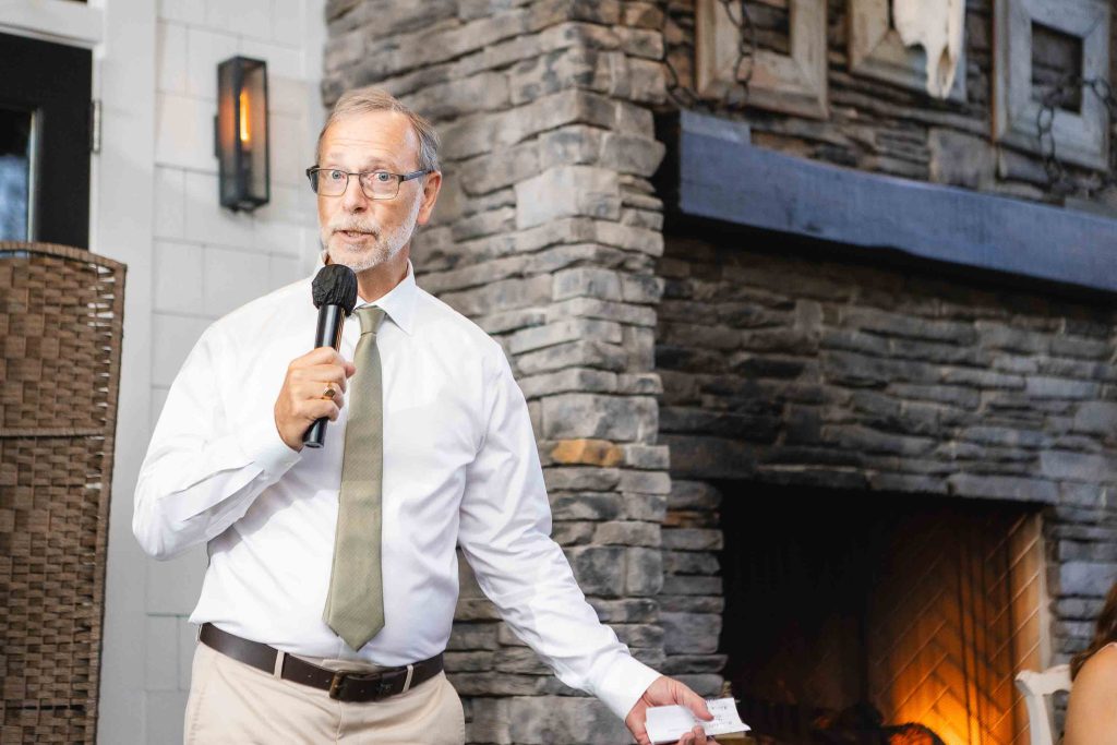 A man giving a speech at a wedding reception in front of a fireplace at Blackwall Barn & Lodge.