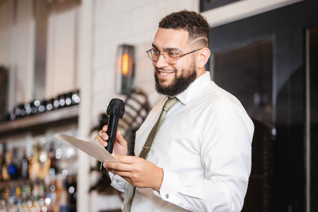 A man holding a microphone at a wedding reception in the Blackwall Barn & Lodge.