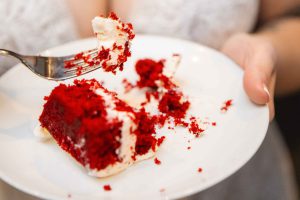 In a wedding ceremony, a bride delicately holds a slice of exquisite red velvet cake, focusing on every delicious detail.