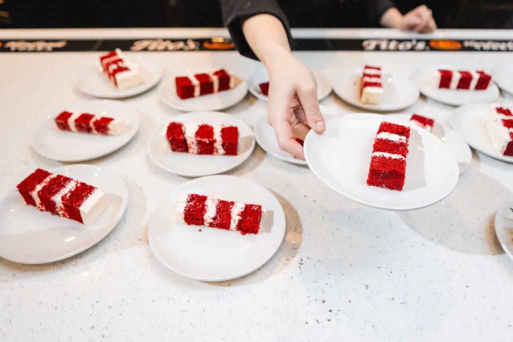 A person is holding a plate of red velvet cake with wedding details.