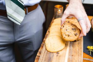 A man is holding cookies in intricate wedding designs on a cutting board.