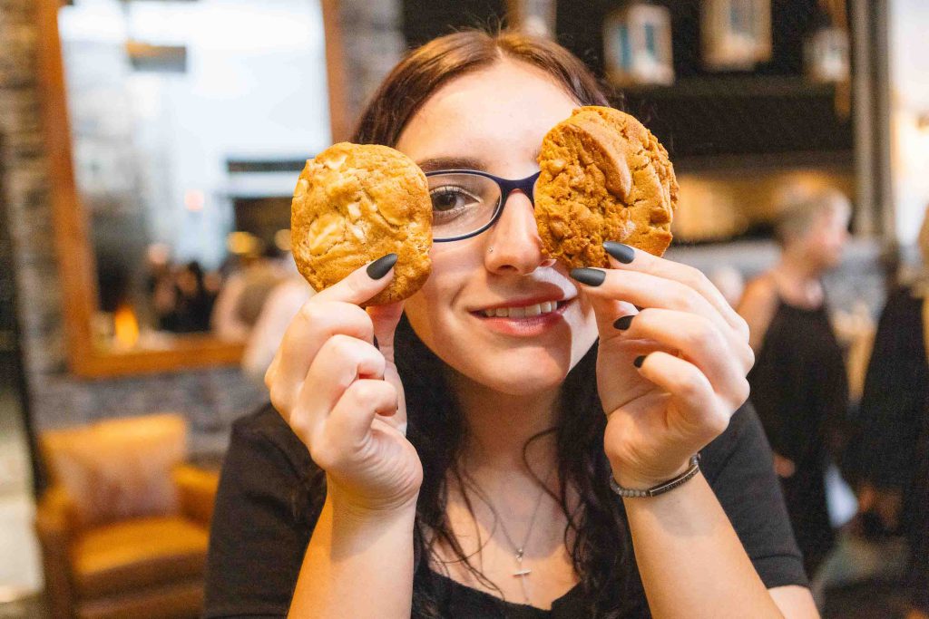 A woman holding two cookies in front of her face at a wedding reception at Blackwall Barn & Lodge.