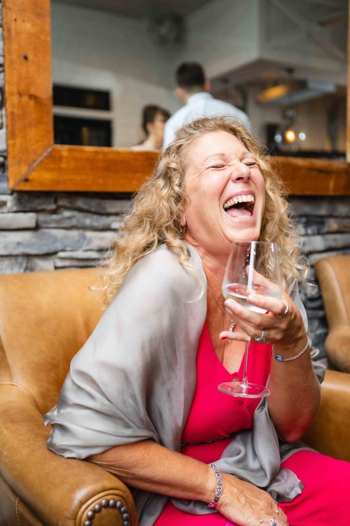 A woman laughing at a wedding reception while holding a glass of wine.
