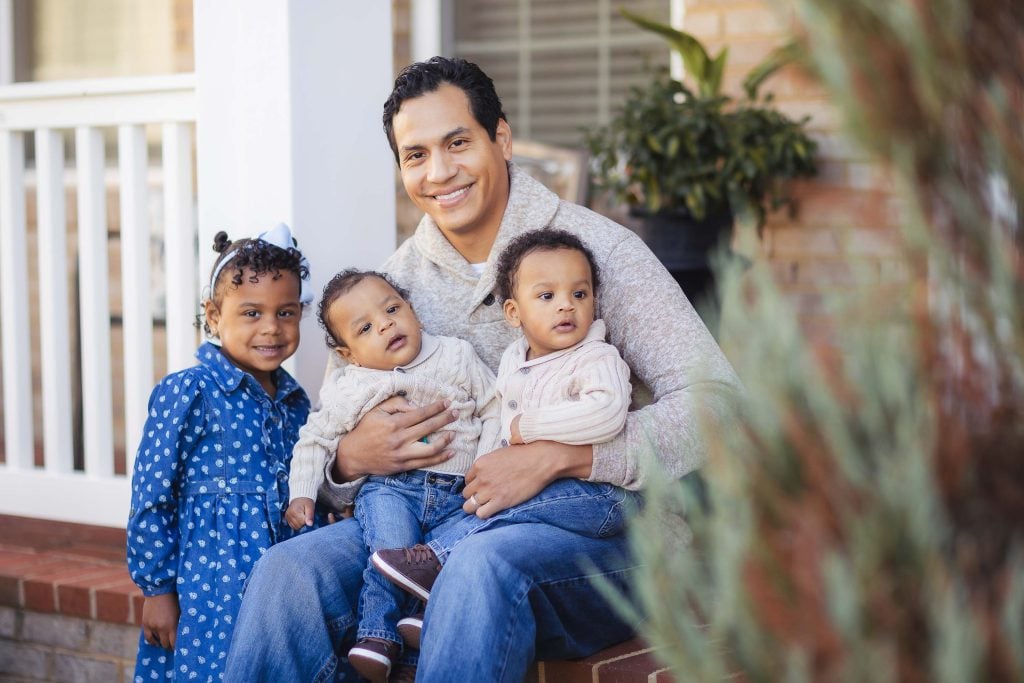 At home, a man and his two children sit on the steps, capturing a heartwarming family portrait.